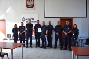 Policjanci na tle ściany z napisem komenda powiatowa policji w szamotułach